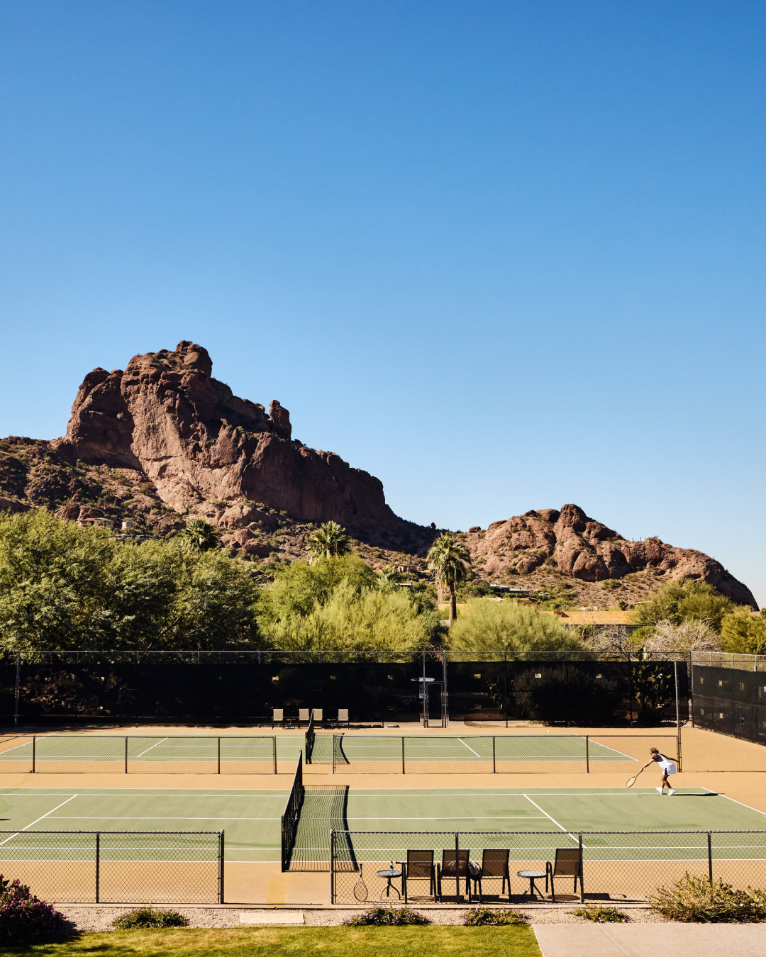 Tennis court surrounded by desert landscape and rocky mountains under a clear blue sky.
