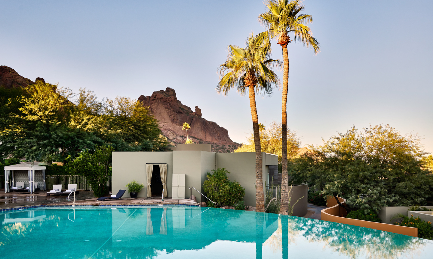 A pool with turquoise water fills the foreground at Sanctuary Camelback Mountain Resort and Spa, Scottsdale, before a cabana and rock ridge.