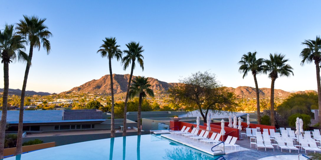 View of Infinity Pool with white lounge chairs and umbrellas as sun sets over mountain in background.