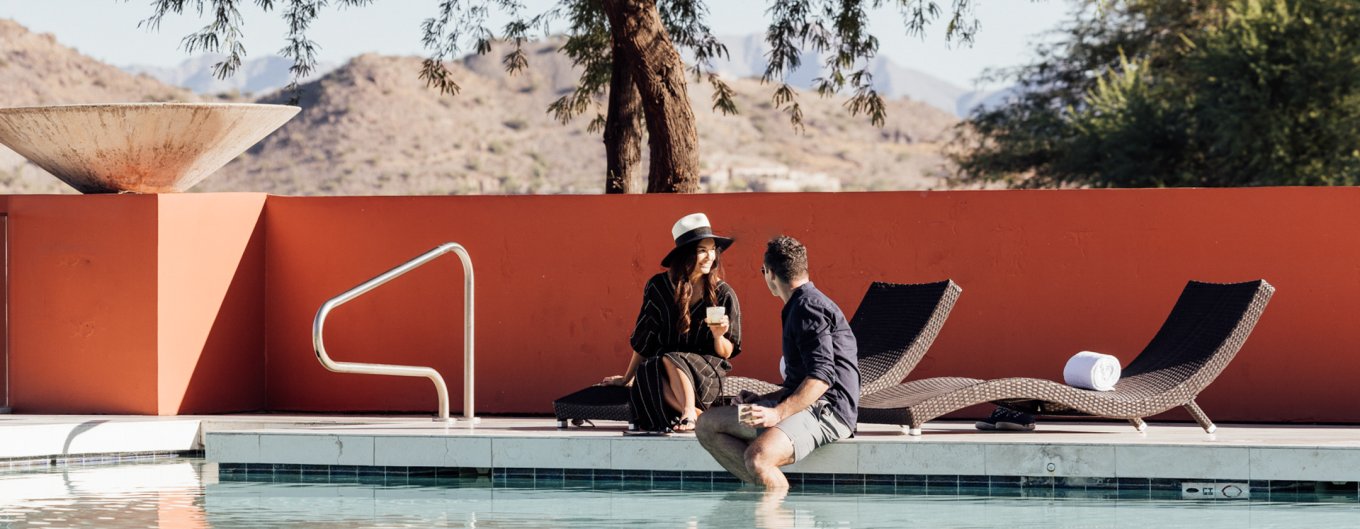 Couple lounging with drinks poolside and feet dangling in Infinity Pool