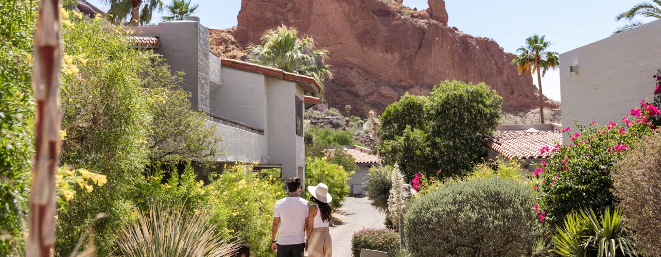 Couple in comfortable attire walking through lush, desert landscape outside Mountain Casitas and Suites.