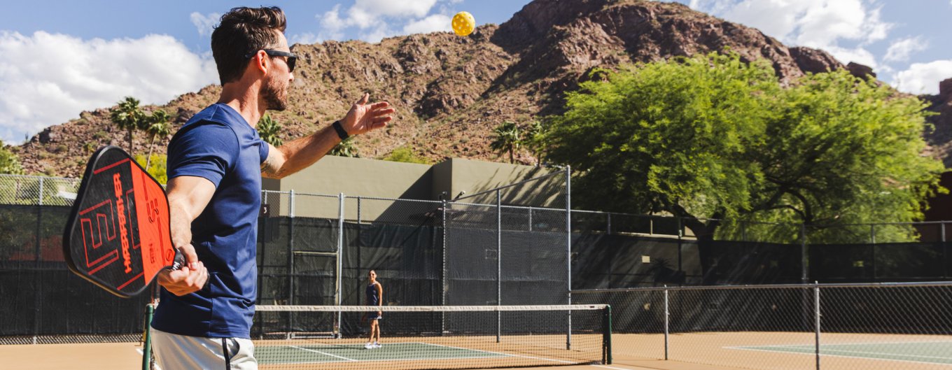 Couple playing Pickleball on Sanctuary's outdoor court with Camelback Mountain in background.