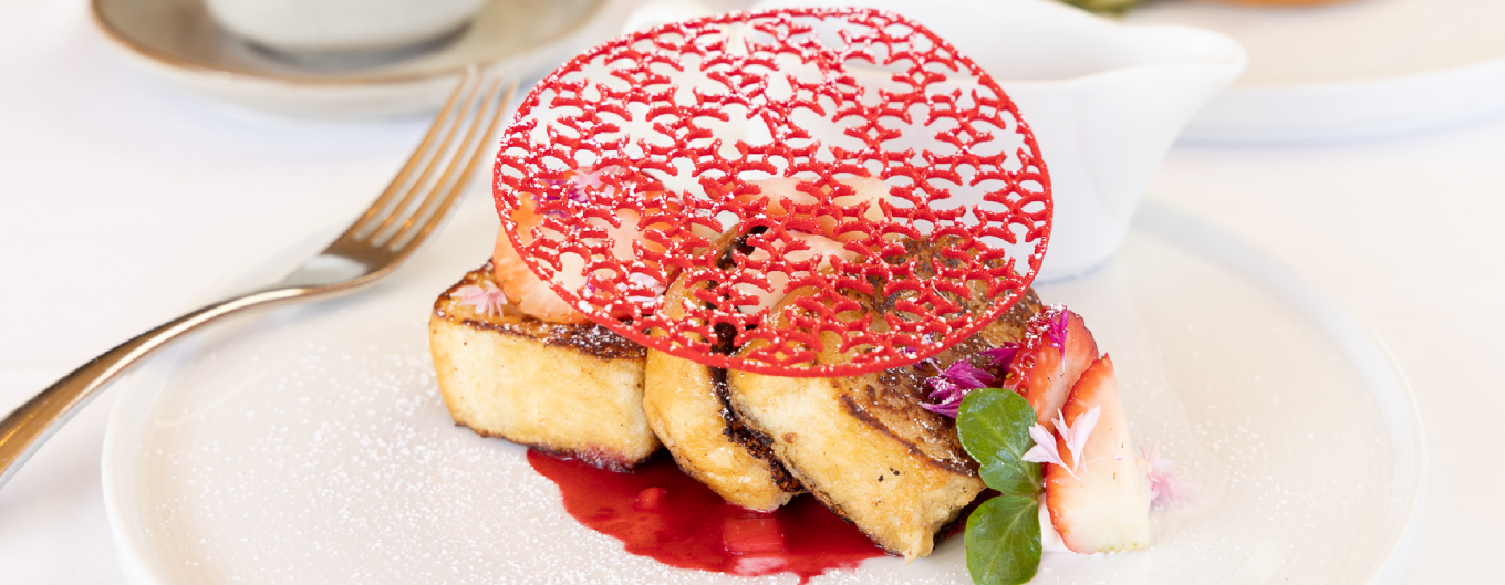 Strawberry waffles with a red lace garnish and strawberry compote on the side against a white tablecloth