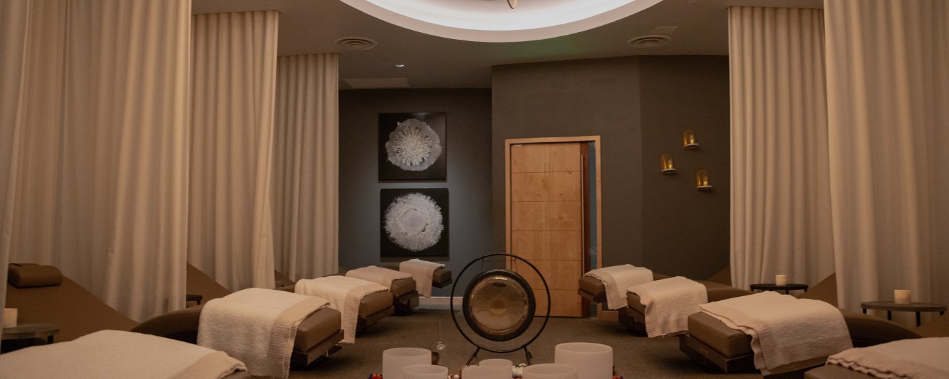 Spa relaxation room with several lounge chairs draped in white towels, warm lighting, and decorative artwork on the walls.