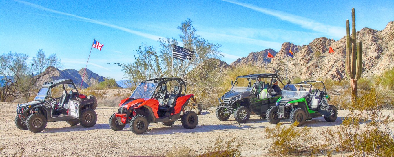 Four dune buggies parked in a desert landscape with cacti and mountains under a clear blue sky.