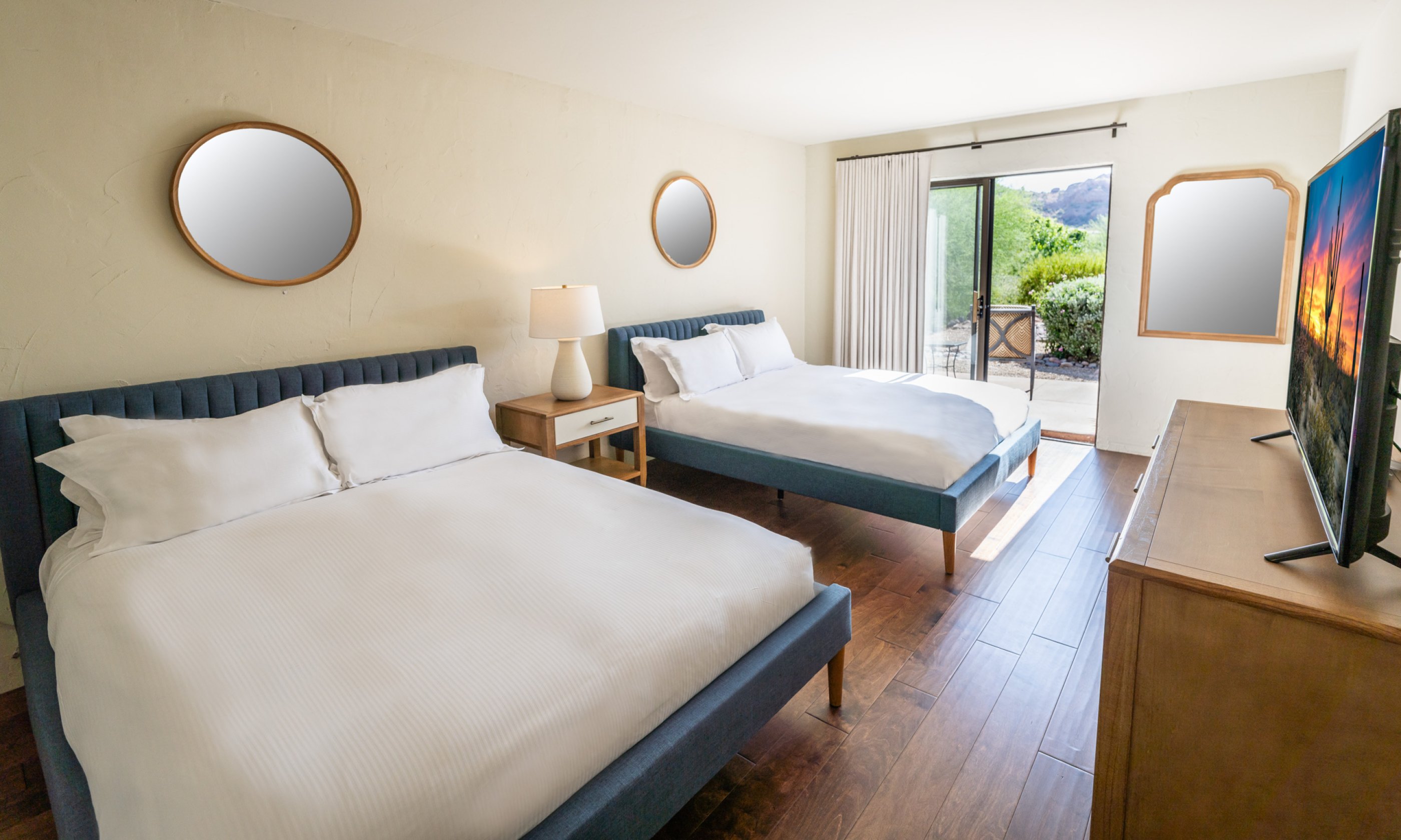 Bedroom with two double beds with blue frames, wood flooring, wooden dresser, flatscreen television and outdoor patio access.