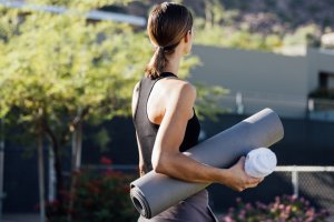Woman in fitness attire with yoga mat walking on Sanctuary's Spa Fitness Lawn.