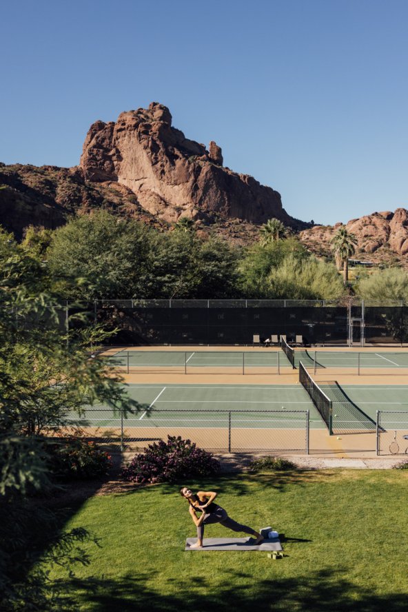 Woman doing yoga on grass in front of tennis courts with view of Praying Monk in the background.