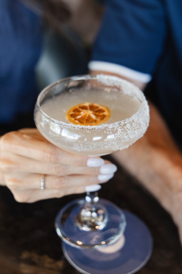 Close up of woman holding cocktail in fine glassware with citrus garnish and sugar-lined rim.
