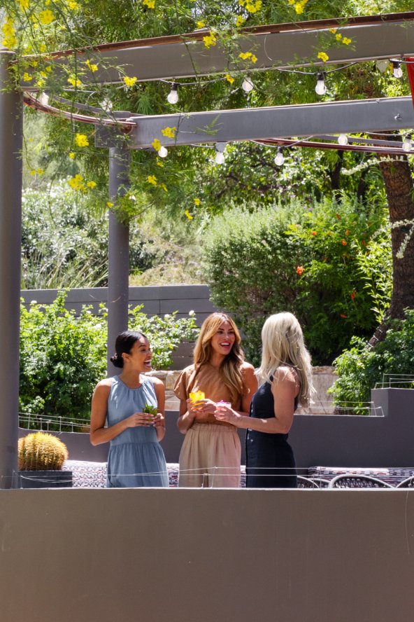 Three girlfriends enjoying craft cocktails and a laugh on jade bar patio surrounded by lush desert landscape.