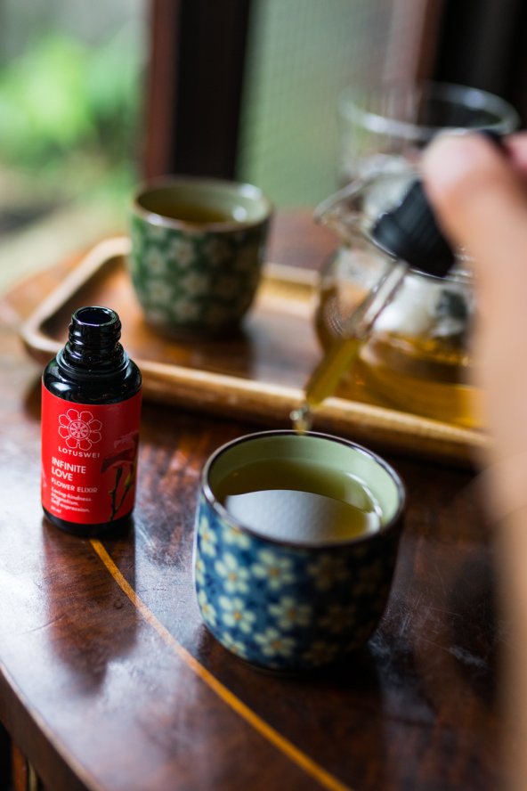 Woman adding drops of LOTUSWEI Infinite Love into tea cup.