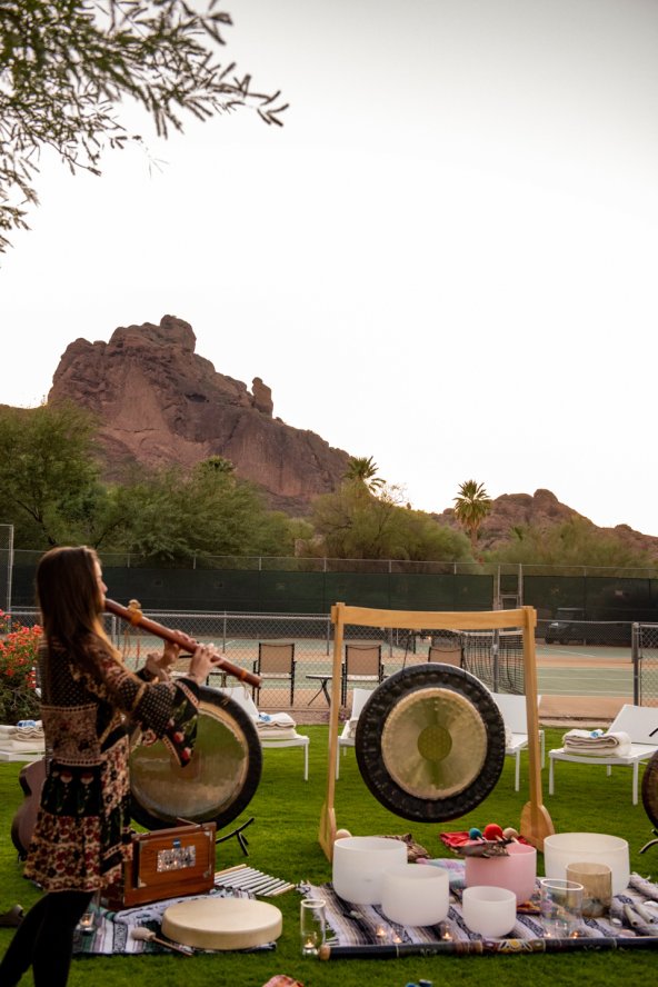 Woman playing flute at outdoor Sound Journey ceremony with Praying Monk in background. 