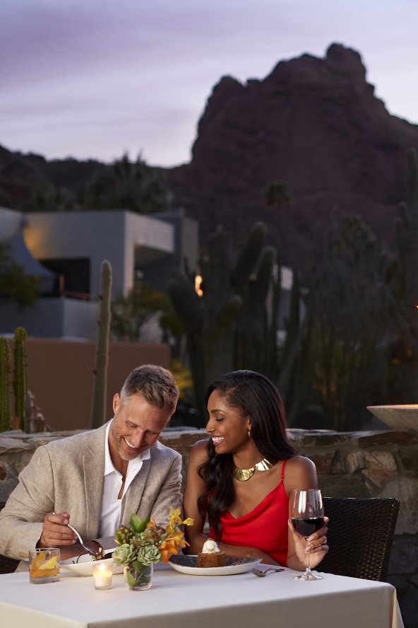A couple enjoys dinner at dusk with Scottsdale's Praying Monk rock formation in the background