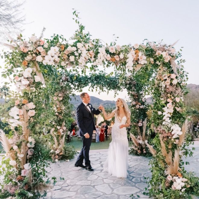 Bride and Groom holding hands under flower canopy.
