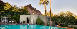 Pool with a mountain view, surrounded by greenery and a palm tree at sunset, with a cabana and lounge chairs to the side.
