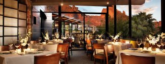 Elegant restaurant interior with candlelit tables and large windows showcasing a view of red rock formations at sunset.