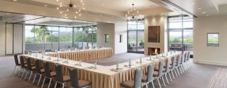 Spacious conference room with U-shaped table, chairs, and natural light from large windows. Chandelier lighting creates a formal setting.